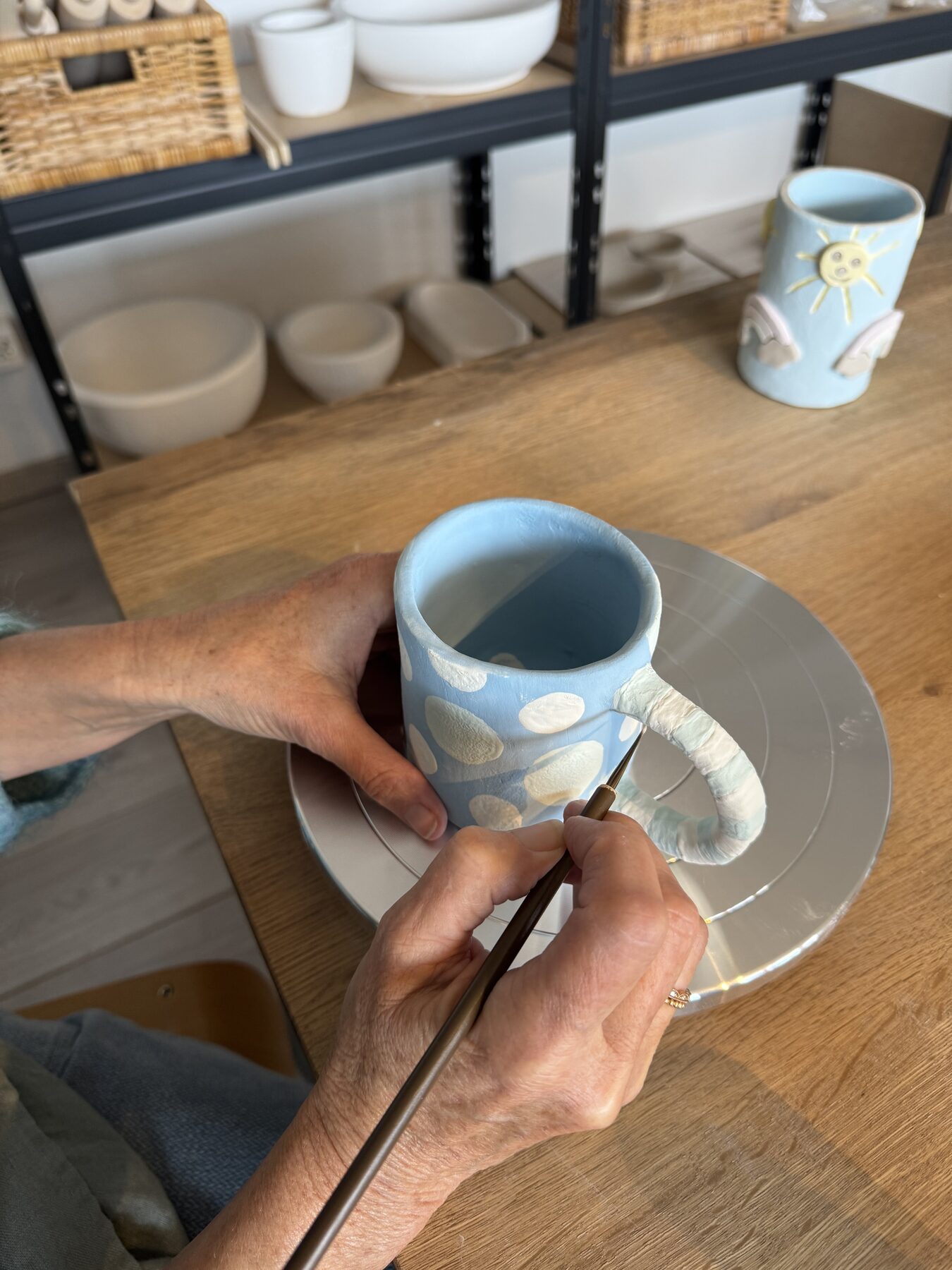Hände bemalen eine hellblaue Tasse mit weissen Tupfen